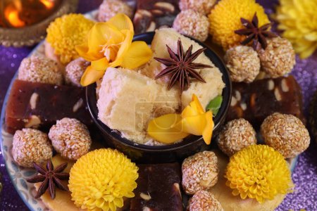 Diwali-Feier. Leckere indische Süßigkeiten, Anissterne und Blumen auf violettem Tisch