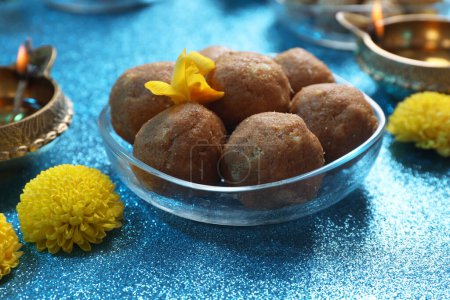 Téléchargez les photos : Fête de Diwali. Fleurs jaunes et savoureux bonbons indiens sur table bleu clair brillant, gros plan - en image libre de droit