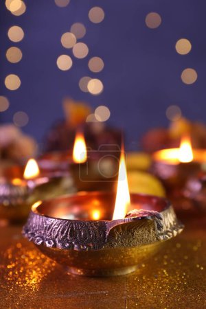 Téléchargez les photos : Fête de Diwali. Lampe Diya sur table dorée brillante contre les lumières floues, gros plan - en image libre de droit