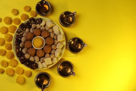 Téléchargez les photos : Joyeux Diwali. Composition à plat avec lampes diya, fleurs de chrysanthème et délicieux bonbons indiens sur table jaune. Espace pour le texte - en image libre de droit
