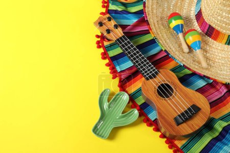 Composition avec chapeau de sombrero mexicain, ukulélé et maracas sur table jaune, vue ci-dessus. Espace pour le texte