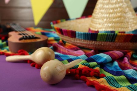 Chapeau sombrero mexicain, poncho et maracas en bois sur table violette, gros plan