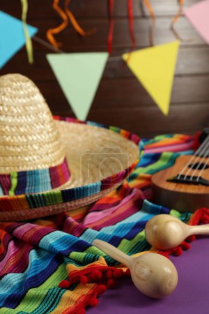 Chapeau sombrero mexicain, ukulélé, poncho et maracas sur table violette, gros plan