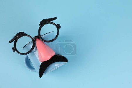 Téléchargez les photos : Visage d'homme en bonnet, fausse moustache, nez et lunettes sur fond bleu clair, vue de dessus. Espace pour le texte - en image libre de droit