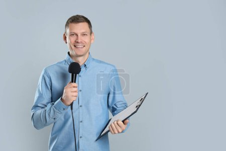 Journaliste masculin avec microphone et presse-papiers sur fond gris. Espace pour le texte
