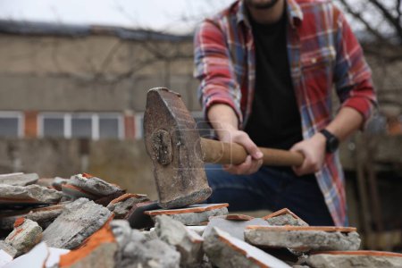 Man breaking bricks with sledgehammer outdoors, selective focus