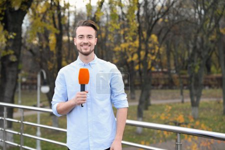 Photo for Young male journalist with microphone working in park - Royalty Free Image