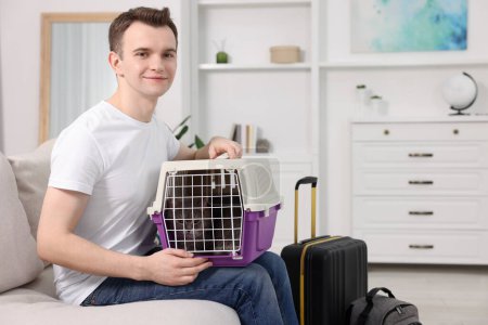 Téléchargez les photos : Voyage avec animal de compagnie. Homme tenant transporteur avec chat mignon sur le canapé à la maison, espace pour le texte - en image libre de droit