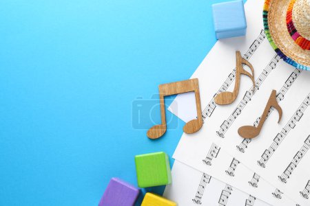 Babylieder. Notenblätter, Holznotizen, Würfel und Hut auf hellblauem Hintergrund, flache Lage mit Platz für Text
