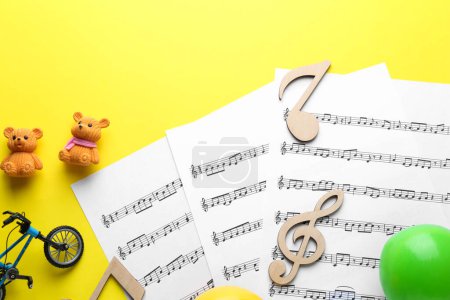 Babylieder. Notenblätter, Holznotizen und verschiedene Spielzeuge auf gelbem Hintergrund, flach gelegt