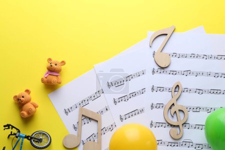 Babylieder. Notenblätter, Holznotizen und verschiedene Spielzeuge auf gelbem Hintergrund, flach gelegt