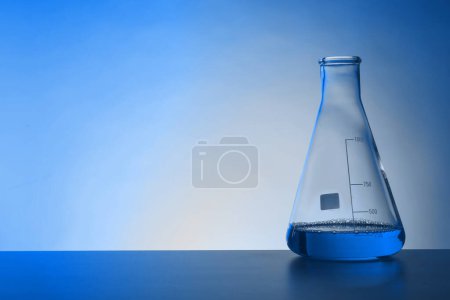 Photo for Conical flask with liquid on table, space for text. Toned in blue. Laboratory glassware - Royalty Free Image