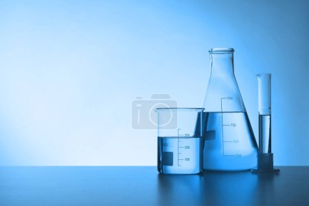 Vidrio de laboratorio con líquido en la mesa, espacio para el texto. Tonificado en azul