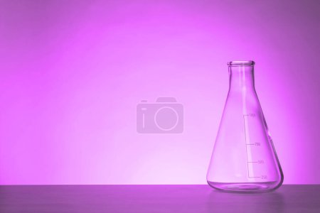 Conical flask with liquid on table, space for text. Toned in violet. Laboratory glassware