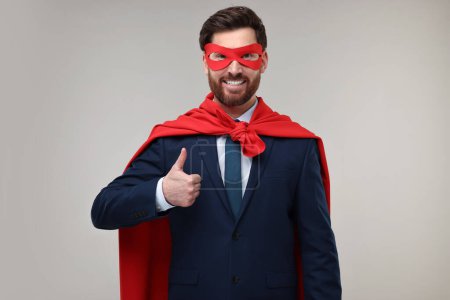 Foto de Feliz hombre de negocios en capa de superhéroe rojo y máscara que muestra los pulgares hacia arriba sobre fondo beige - Imagen libre de derechos