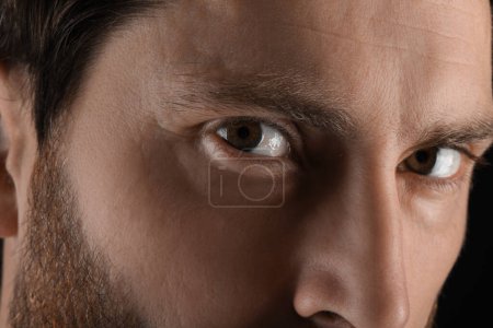 Photo for Evil eye. Man with scary eyes on black background, closeup - Royalty Free Image