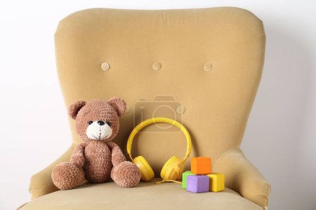 Babylieder. Spielzeugbär, Kopfhörer und Würfel auf Sessel nahe weißer Wand