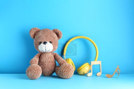 Babylieder. Spielzeugbär, gelbe Kopfhörer und Holznotizen auf hellblauem Hintergrund