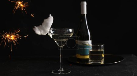 Cocktail with tasty cotton candy and bottle of alcohol drink on dark textured table