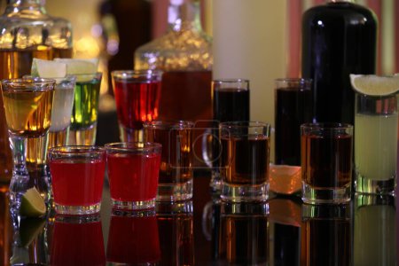 Different shooters in shot glasses and bottles on mirror surface. Alcohol drink