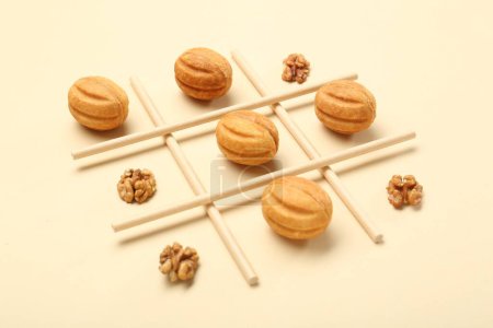 Tic tac toe game made with walnuts and cookies on beige background