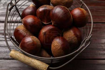 Marrons comestibles frais sucrés dans un panier en métal sur une table en bois, gros plan