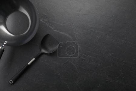 Photo for Black metal wok and spatula on dark textured table, top view. Space for text - Royalty Free Image