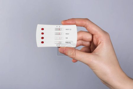 Frau mit Einweg-Multiinfektionstest auf hellgrauem Hintergrund, Nahaufnahme