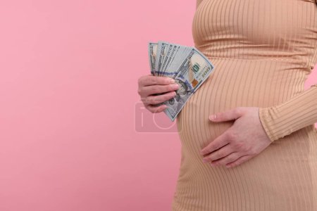 Téléchargez les photos : Mère porteuse. Femme enceinte avec des billets en dollars sur fond rose, gros plan. Espace pour le texte - en image libre de droit