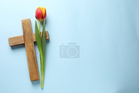 Photo for Easter - celebration of Jesus resurrection. Wooden cross and tulip on light blue background, top view. Space for text - Royalty Free Image