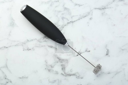 Black milk frother wand on white marble table, top view