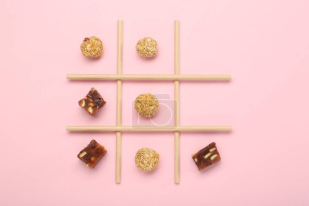 Tic Tac Toe Spiel mit Süßigkeiten auf rosa Hintergrund, Ansicht von oben