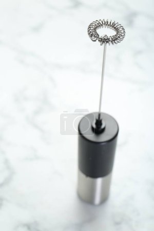 Black milk frother wand on white marble table