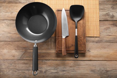 Photo for Black metal wok, knife and spatula on wooden table, top view - Royalty Free Image
