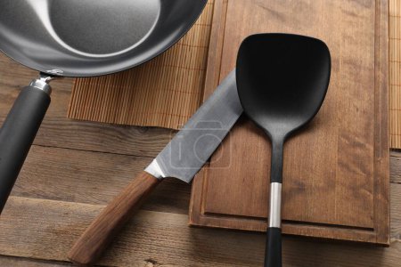 Photo for Black metal wok, knife and spatula on wooden table, above view - Royalty Free Image
