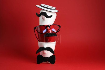 Téléchargez les photos : Visages d'hommes faits de tasses, faux moustaches, lunettes, chapeau et noeud papillon sur fond rouge - en image libre de droit