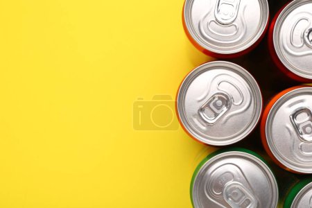 Energy drink in cans on yellow background, top view. Space for text