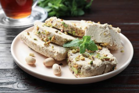 Pieces of tasty halva with pistachios and mint on wooden table, closeup