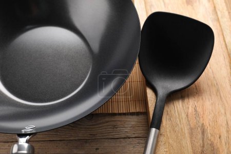 Black metal wok and spatula on wooden table, closeup
