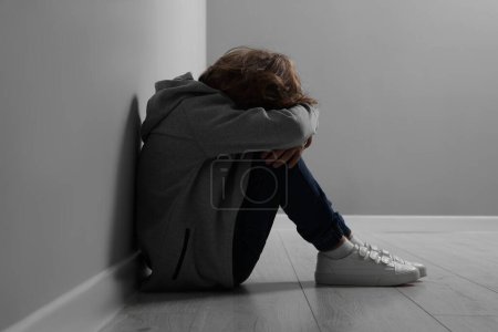 Kindesmissbrauch. Aufgebrachter Junge sitzt auf dem Boden neben grauer Wand