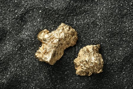 Photo for Shiny gold nuggets on black sand, top view - Royalty Free Image