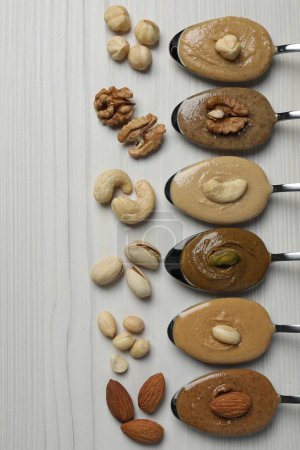 Photo for Tasty nut butters in spoons and raw nuts on white wooden table, flat lay - Royalty Free Image