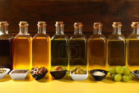 Foto de Grasas vegetales. Diferentes aceites en botellas de vidrio e ingredientes en mesa amarilla - Imagen libre de derechos