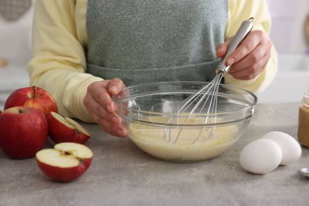 Woman whisking eggs in bowl at grey table indoors, closeup