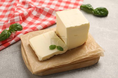 Block of tasty butter with basil on grey table
