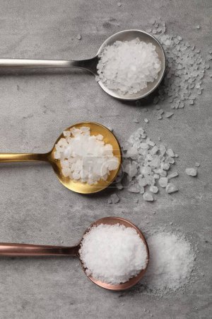 Natürliches Salz in Löffeln auf grauem Tisch, flach gelegt
