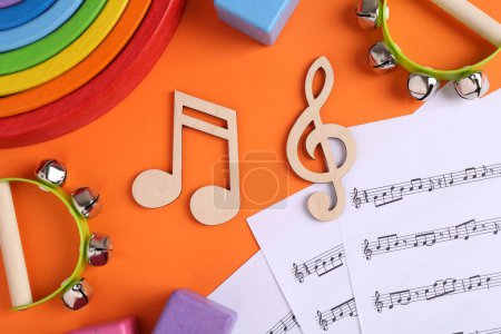Werkzeuge zum Erstellen von Babyliedern. Flache Komposition mit hölzernen Noten und Tamburinen für Kinder auf orangefarbenem Hintergrund