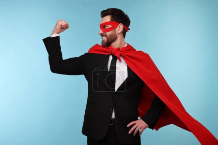 Hombre de negocios con capa de superhéroe rojo y máscara sobre fondo azul claro