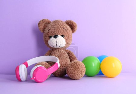 Babylieder. Spielzeugbär, Kopfhörer und Kugeln auf violettem Hintergrund