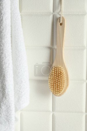 Accesorios de baño. Cepillo de bambú y toalla de rizo en pared de azulejos blancos